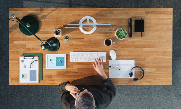 A top view of businessman working on computer at desk with paperwork in home office.