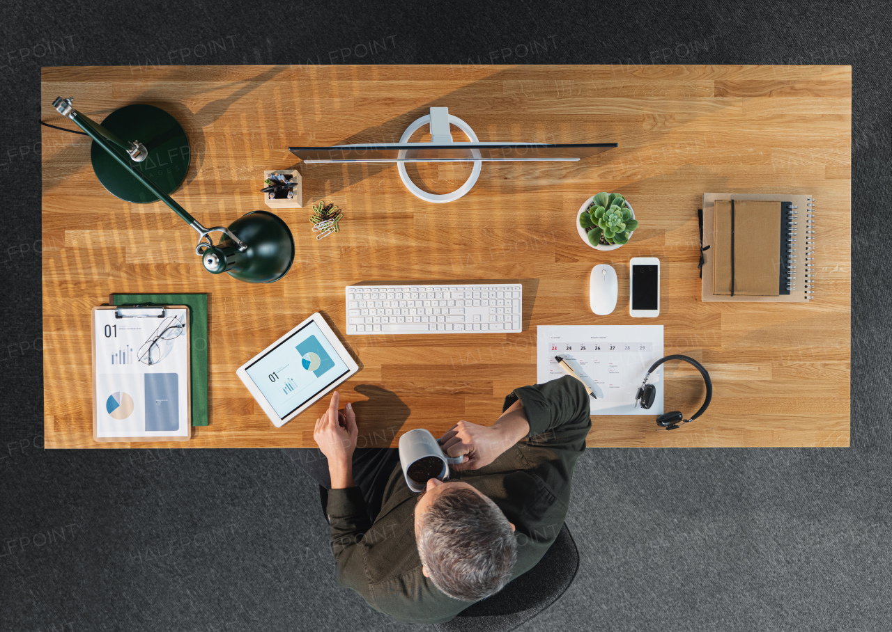 A top view of businessman working on computer at desk with paperwork in home office.