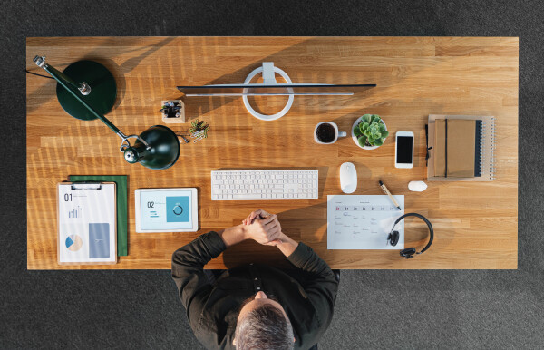 A top view of businessman working on computer at desk with paperwork in home office.