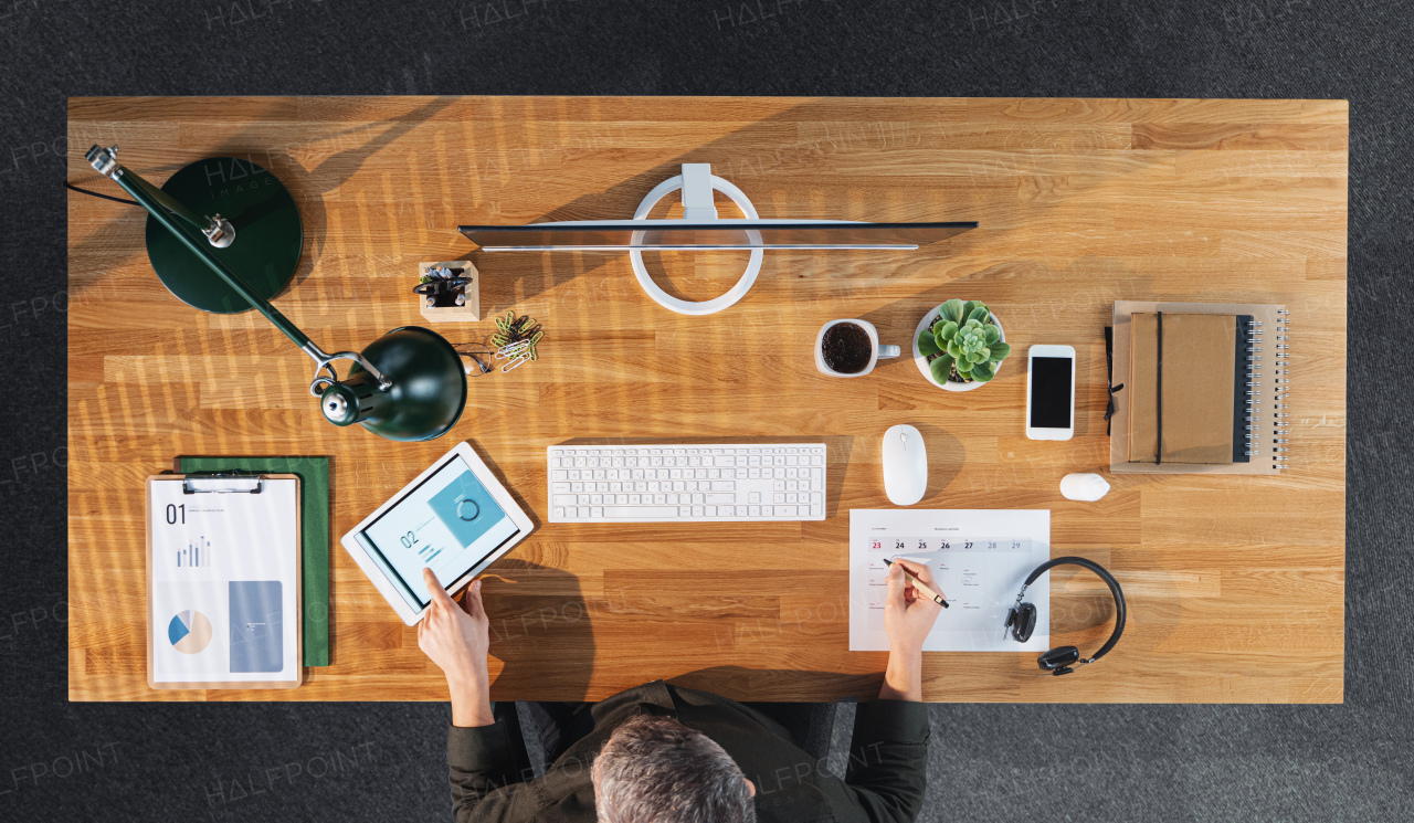 A top view of businessman working on computer at desk with paperwork in home office.