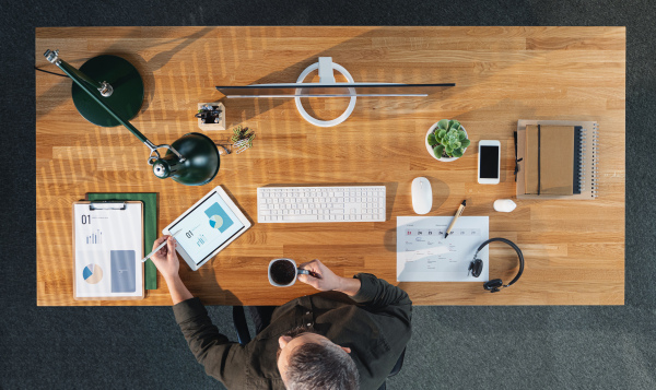 A top view of businessman working on computer at desk with paperwork in home office.