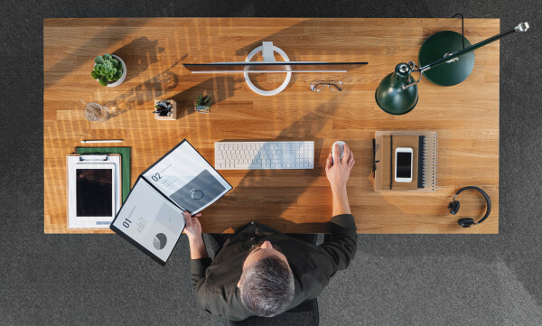 A top view of businessman working on computer at desk with paperwork in home office.