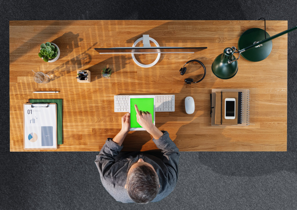 Top view of mature businessman working on computer at desk with keyable screen in home office.