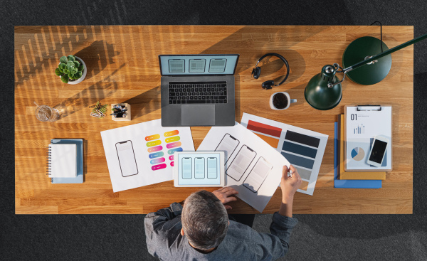 A top view of creative businessman working on laptop computer at desk with paperwork in home office.