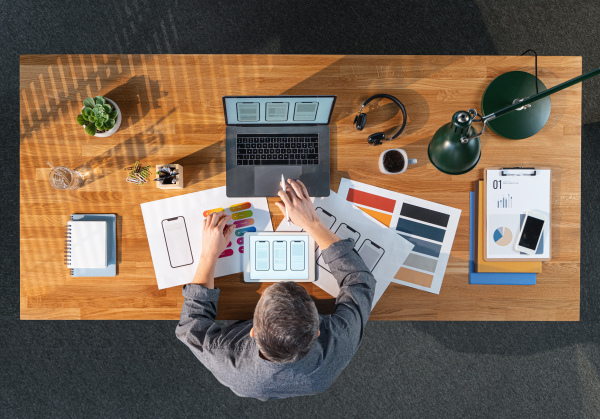 A top view of creative businessman working on laptop computer at desk with paperwork in home office.