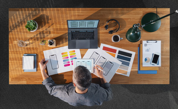 A top view of businessman working on laptop computer at desk with paperwork in home office.