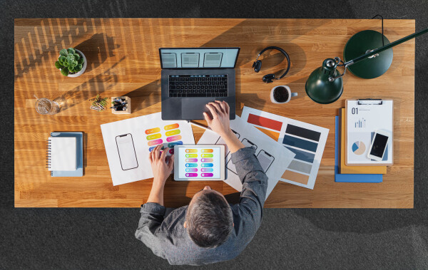 A top view of businessman working on laptop computer at desk with paperwork in home office.