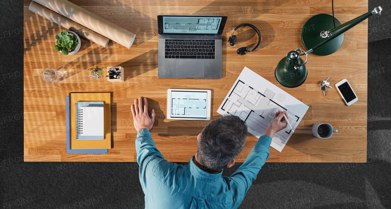 A top view of businessman architect working on laptop computer at desk with paperwork in home office.