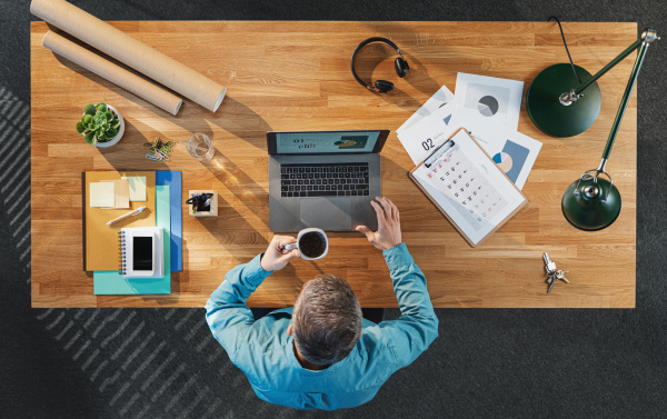 A top view of businessman working on laptop computer at desk with paperwork in home office.