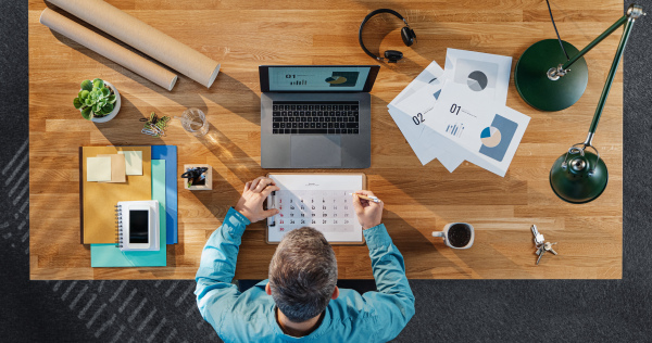 A top view of businessman working on computer at desk with paperwork in home office.