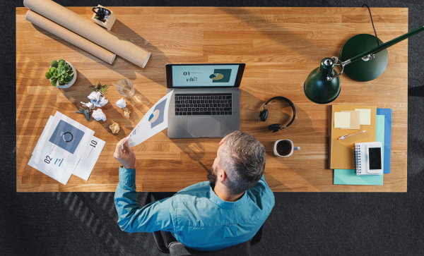 Top view of tired and frustrated businessman working on computer at desk with paperwork in home office.