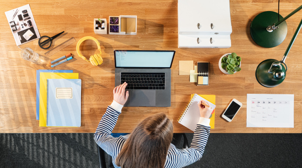 A top view of female student working on computer at desk at home.