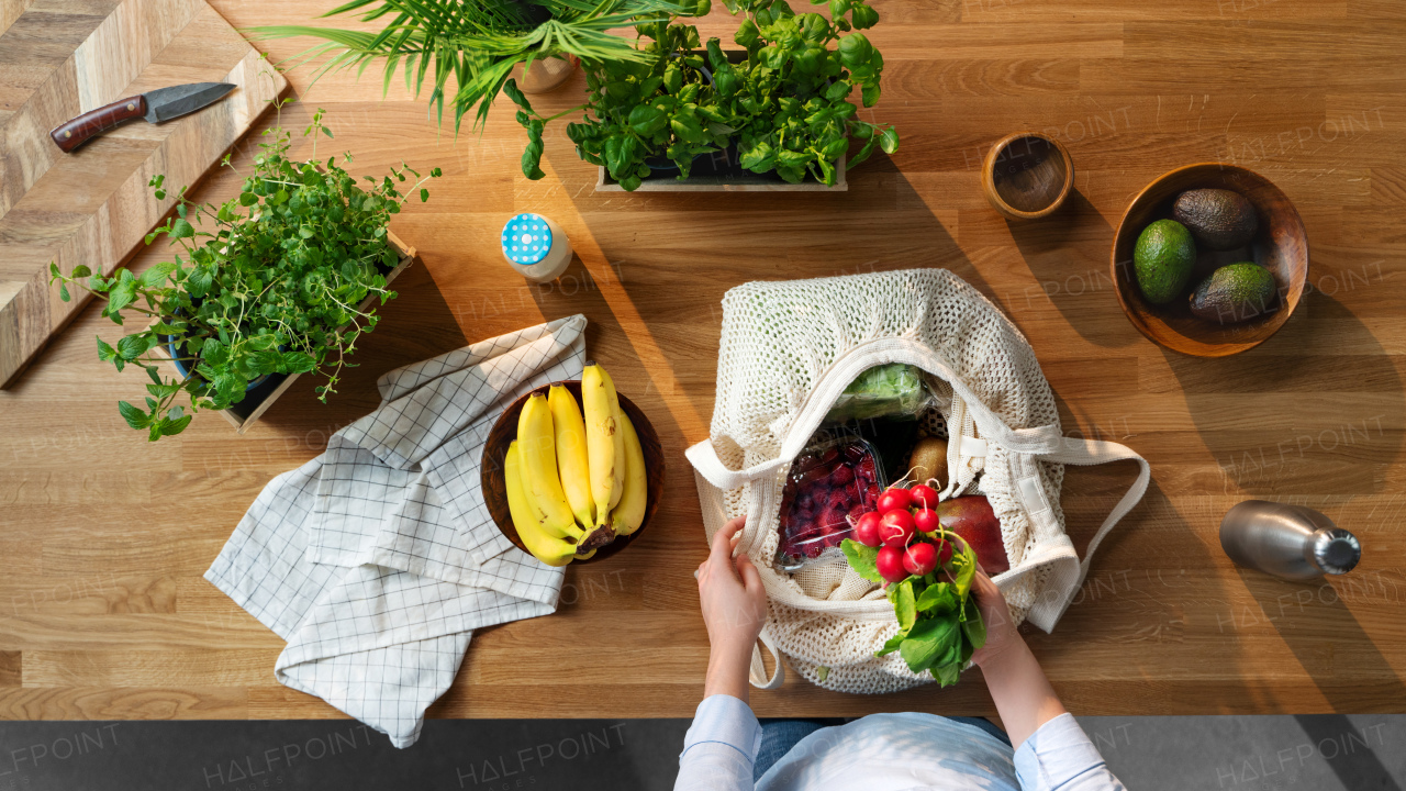 Top view of unrecognizable woman unpacking shopping for fruit and vegetables, sustainable lifestyle.