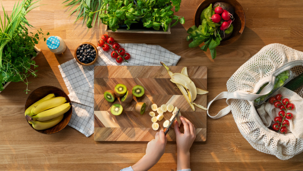 A top view of unrecognizable woman preparing and chopping fruit, sustainable lifestyle.