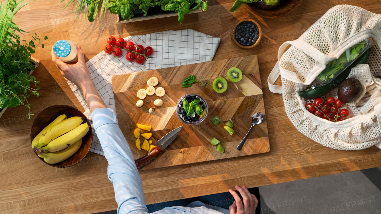 A top view of unrecognizable woman preparing fruit smoothie, sustainable lifestyle.