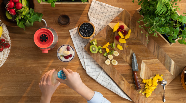 A top view of unrecognizable woman preparing fruit milk shake, sustainable lifestyle.