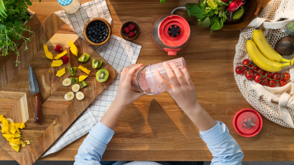 A top view of unrecognizable woman preparing fruit milk shake, sustainable lifestyle.