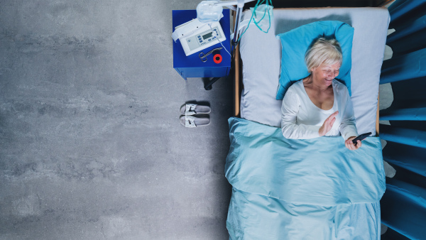 Top view of woman patient using smartphone in bed in hospital, video call with relatives concept.