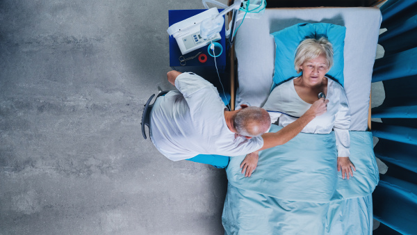 A top view of doctor with stethoscope examining patient in bed in hospital. Copy space.