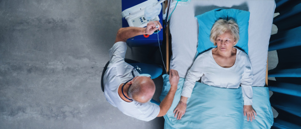 A top view of doctor and woman patient with iv drip in bed in hospital.