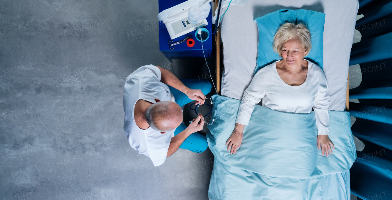 A top view of doctor with stethoscope examining patient in bed in hospital. Copy space.