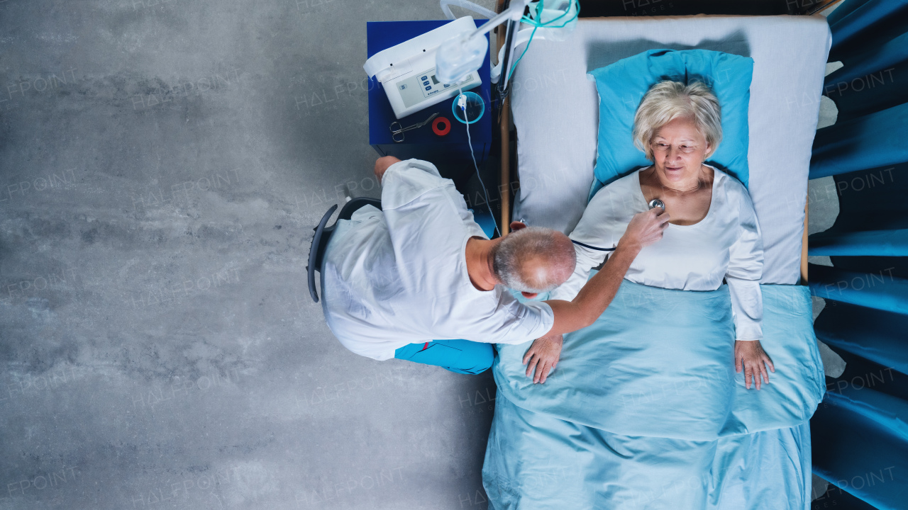 A top view of doctor with stethoscope examining patient in bed in hospital. Copy space.