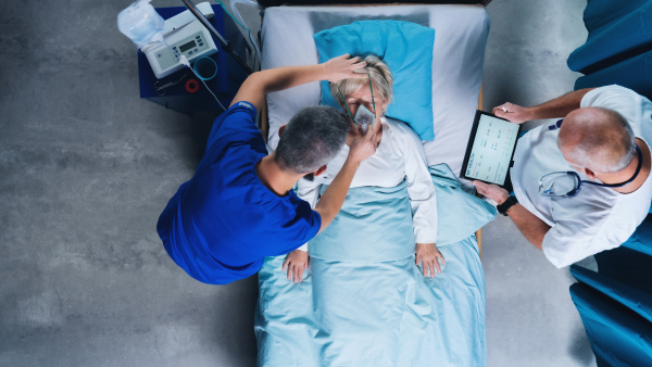 Top view of doctors and infected covid-19 patient with oxygen mask in bed in hospital, coronavirus concept.