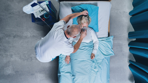 Top view of doctor and infected covid-19 patient with oxygen mask in bed in hospital, coronavirus concept.