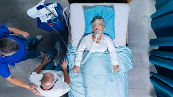 Top view of doctors and infected covid-19 patient with oxygen mask in bed in hospital, coronavirus concept.