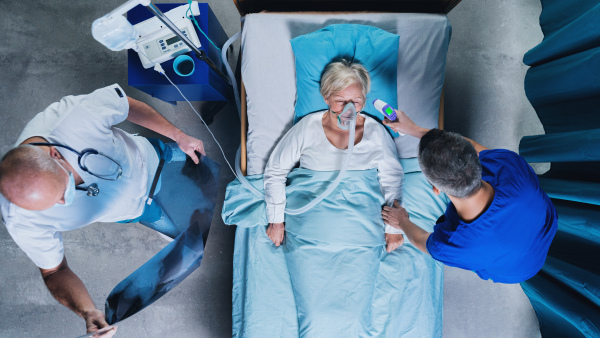 Top view of doctors and infected covid-19 patient with oxygen mask in bed in hospital, coronavirus concept.