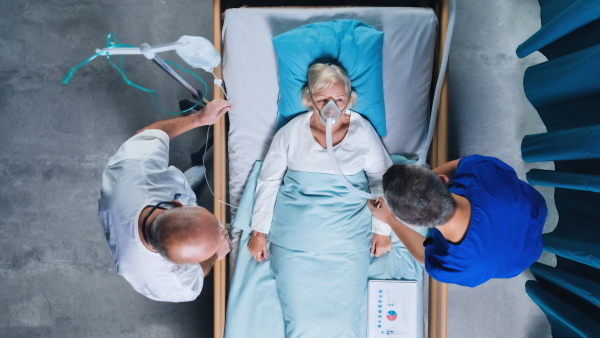 Top view of doctors and infected covid-19 patient with oxygen mask in bed in hospital, coronavirus concept.