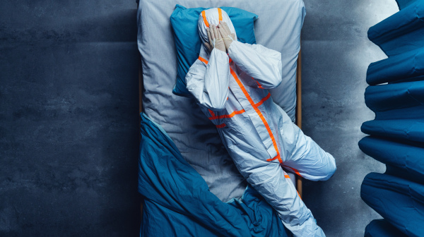 Top view of frustrated doctor in protective suit lying on bed in hospital, coronavirus concept.