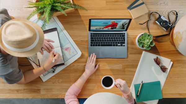 Top view of unrecognizable young couple with laptop and maps planning vacation trip holiday, desktop travel concept.