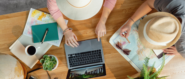 Top view of unrecognizable young couple with laptop and maps planning vacation trip holiday, desktop travel concept.