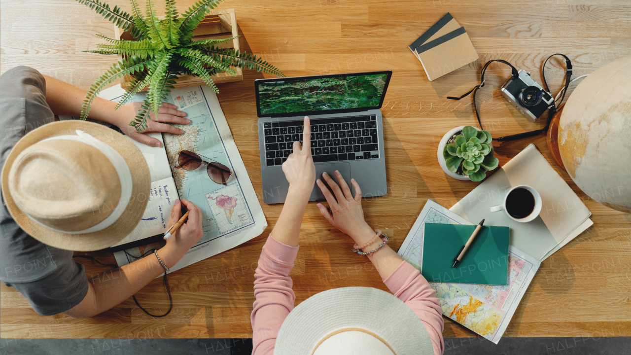 Top view of unrecognizable young couple with laptop and maps planning vacation trip holiday, desktop travel concept.