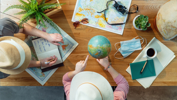 Top view of unrecognizable young couple with maps planning vacation trip holiday, desktop travel concept.