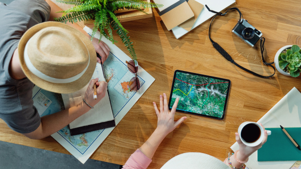 Top view of unrecognizable young couple with tablet and maps planning vacation trip holiday, desktop travel concept.