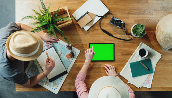 Top view of unrecognizable young couple with tablet and maps planning vacation trip holiday, desktop travel chroma key concept.