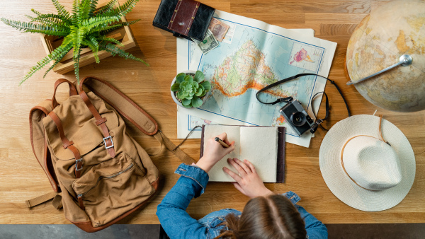 Top view of unrecognizable young woman with maps planning vacation trip holiday, desktop travel concept.