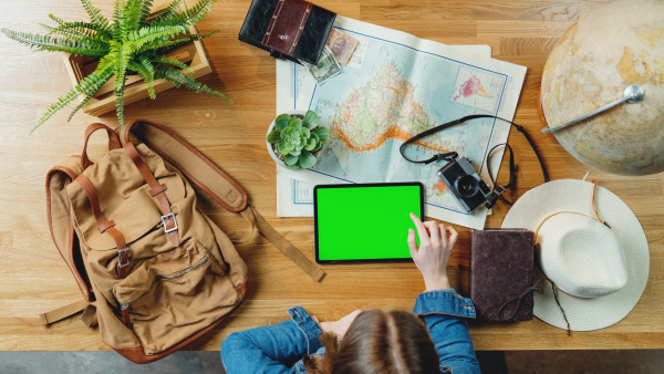 Top view of unrecognizable young woman with tablet and maps planning vacation trip holiday, desktop travel chroma key concept.