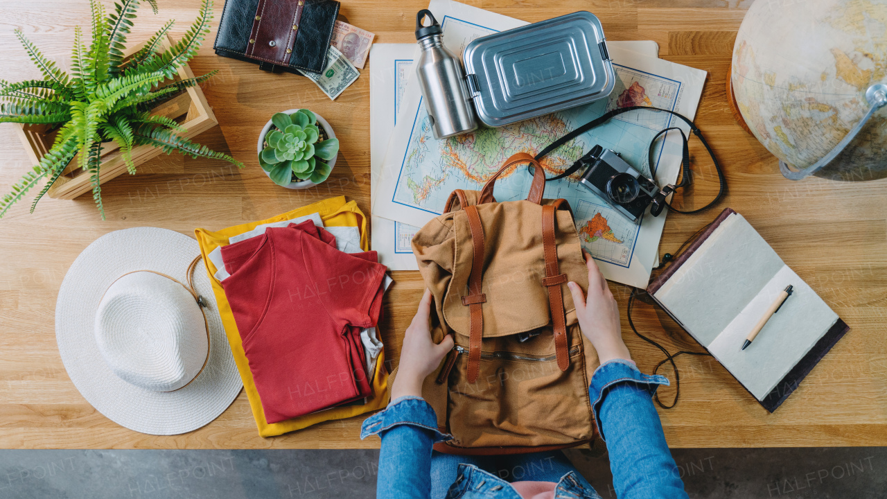 Top view of young woman packing backpack for vacation trip holiday, desktop travel concept.