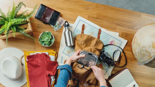 Top view of young woman packing backpack for vacation trip holiday, desktop travel concept.