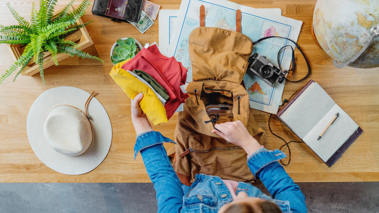 Top view of young woman packing backpack for vacation trip holiday, desktop travel concept.