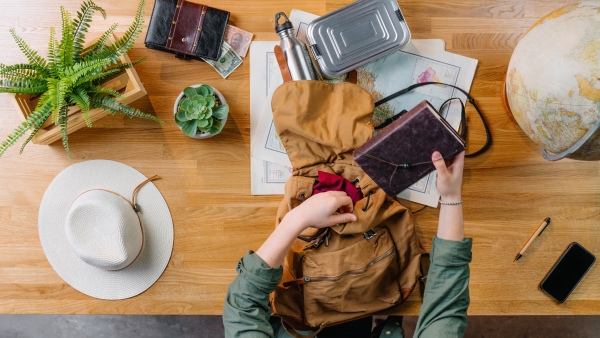 Top view of young woman packing backpack for vacation trip holiday, desktop travel concept.