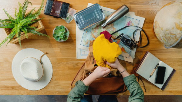 Top view of young woman packing backpack for vacation trip holiday, desktop travel concept.