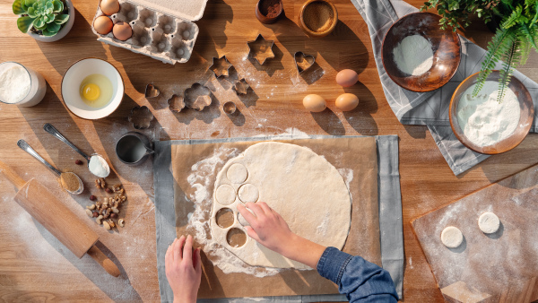 A top view of unrecognizable woman baking biscuits, desktop concept.