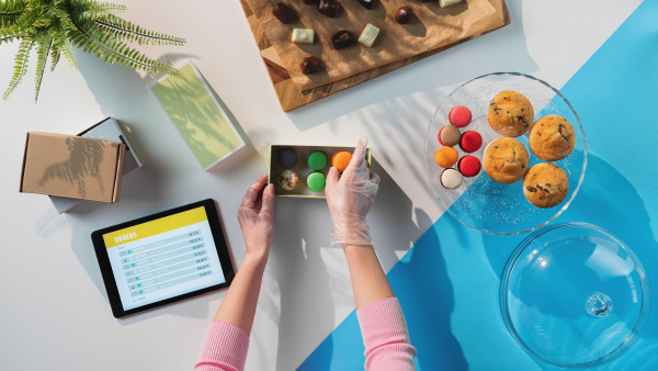 A top view of unrecognizable woman packing biscuits, processing orders desktop concept.