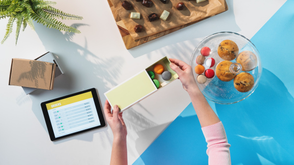 A top view of unrecognizable woman packing biscuits, processing orders desktop concept.