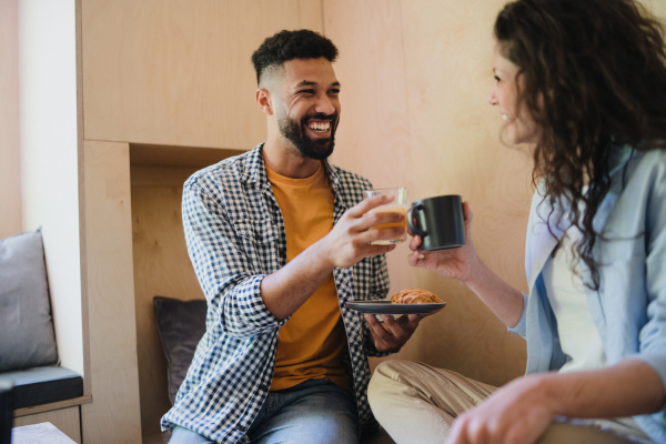 A happy couple in love sitting, resting and drinking coffee indoors in a tree house, weekend away and digital detox concept.