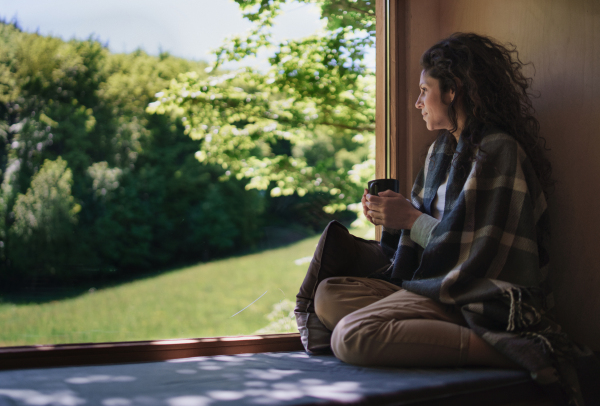 A happy mid adult woman with coffee sitting indoors in a tree house, weekend away and digital detox concept.